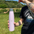 Žena drží pastelovo fialovú termosku Wisteria – detail farby a dizajnu na prírodnom pozadí
