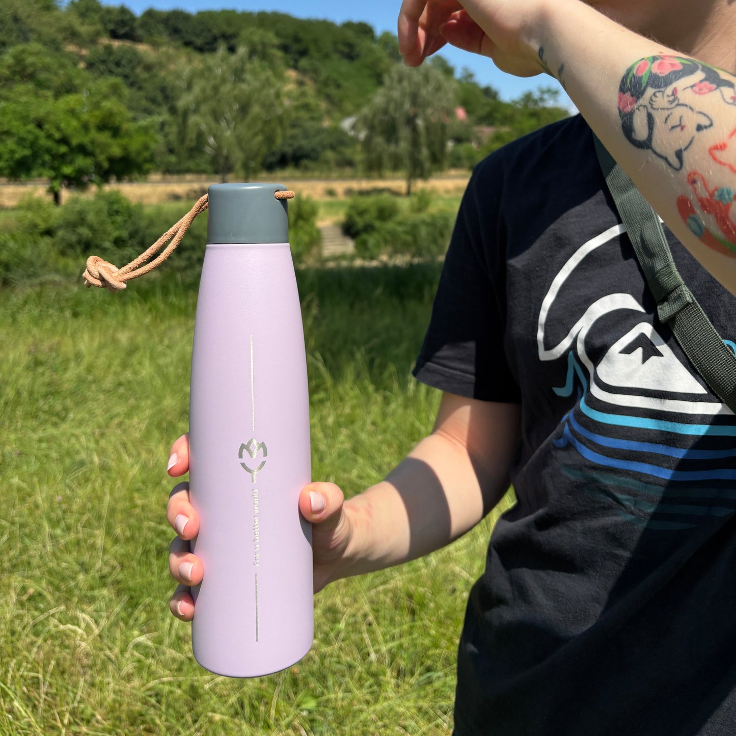 Žena drží pastelovo fialovú termosku Wisteria – detail farby a dizajnu na prírodnom pozadí
