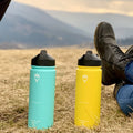  Termoska pre deti 500ml (Slnecnica) položená na kopci vedľa jasne modrej fľaše, bez prítomnosti ľudí, v pozadí hory, zvýraznené využitie a predstava


