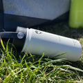  Termoska so slamkou 500ML (biela) položená v tráve, zvýraznený dizajn a farba fľaše, pozadie tvorí prírodná krajina