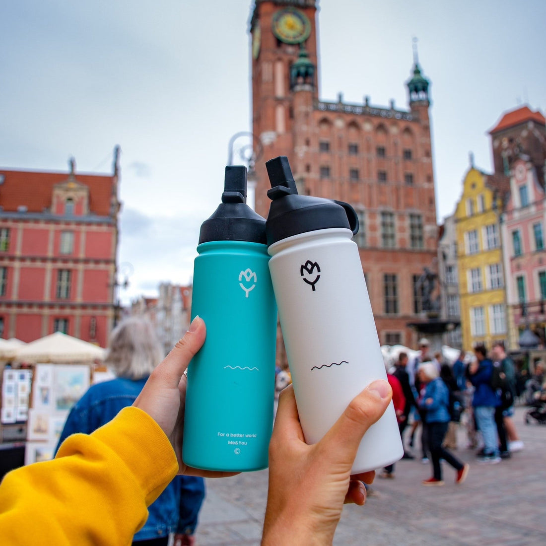  Termoska so slamkou 500ML (biela) držaná mladým mužom, smerom k fotoaparátu, zvýraznená farba fľaše a spôsob držania, pozadie tvorí jazero a slnečné počasie