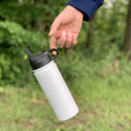 Termoska so slamkou 500ML (biela) držaná za viečko, visí vo vzduchu, zvýraznená funkčnosť viečka, pozadie tvorí les