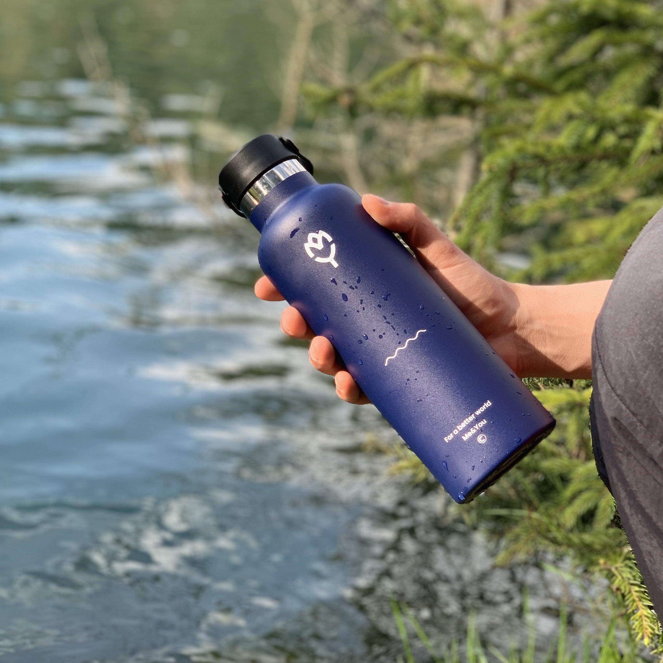 Termoska Glaucus 750ML držaná v ruke, zvýraznená farba a telo fľaše, pozadie tvorí jazero